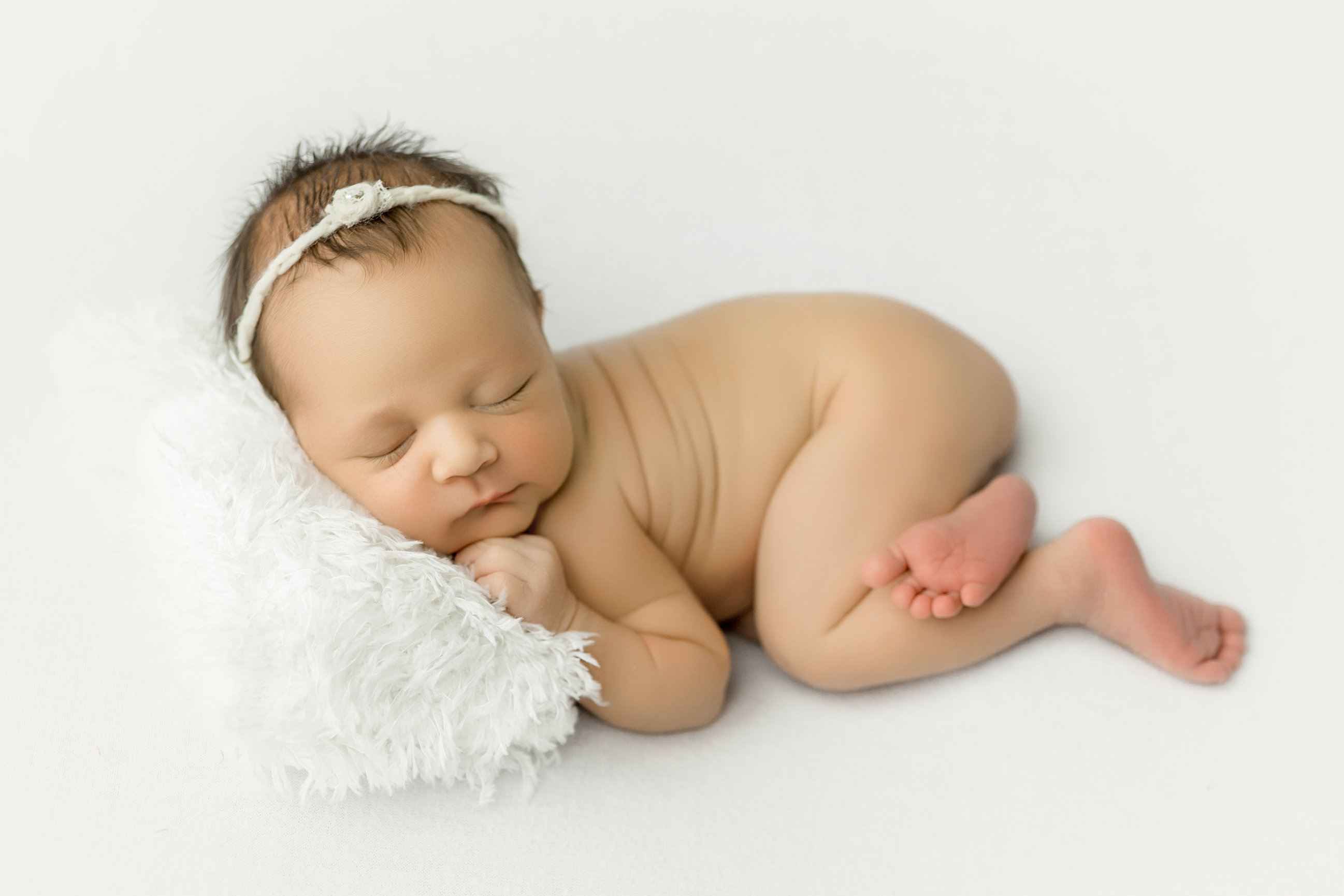 A brand new baby girl asleep on white, one hand curled beneath her cheek.
