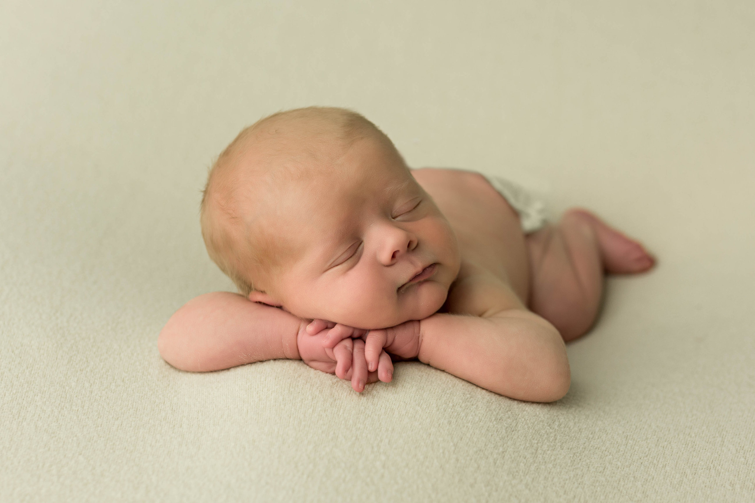 The classic newborn pose, both hands stacked under a sleeping chin.
